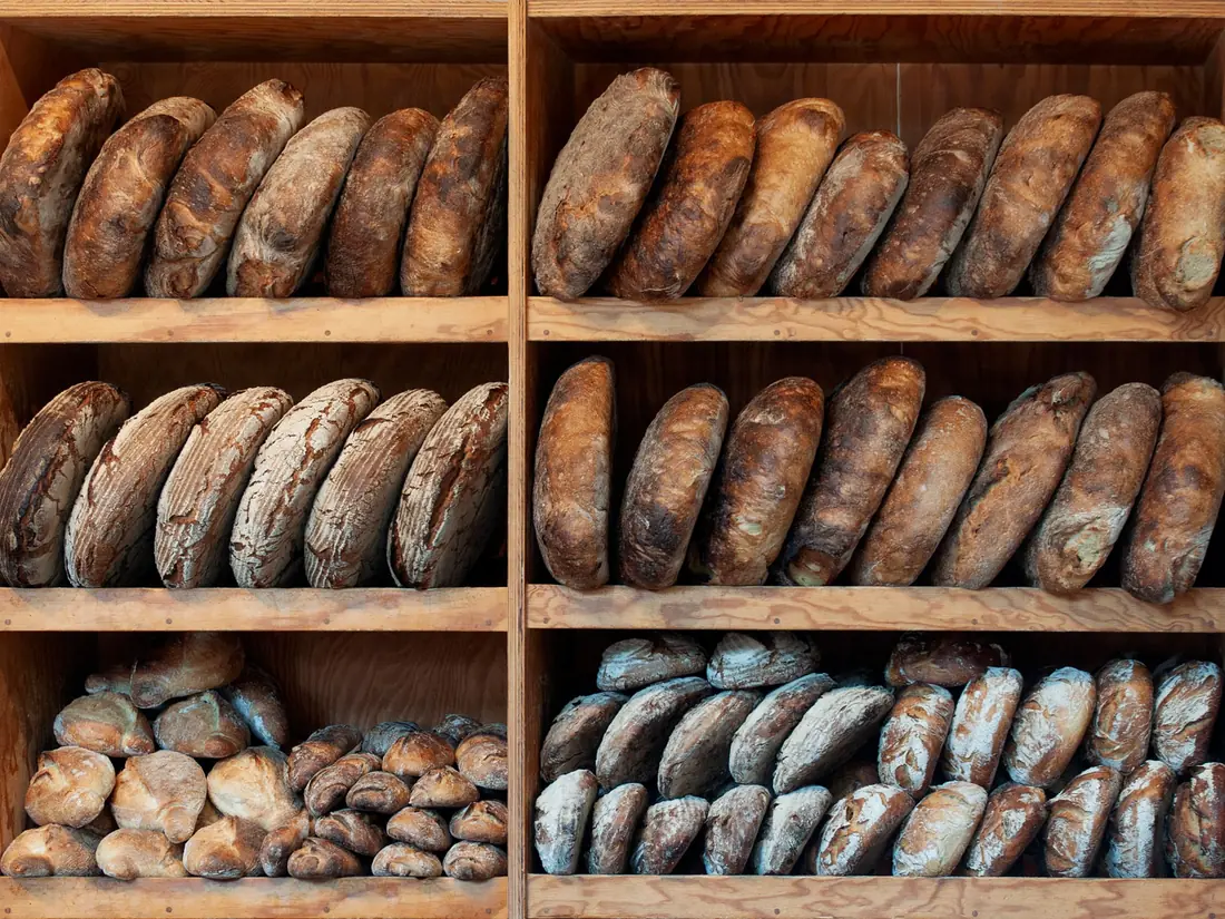 Wooden shelves stacked with dark sourdough loaves