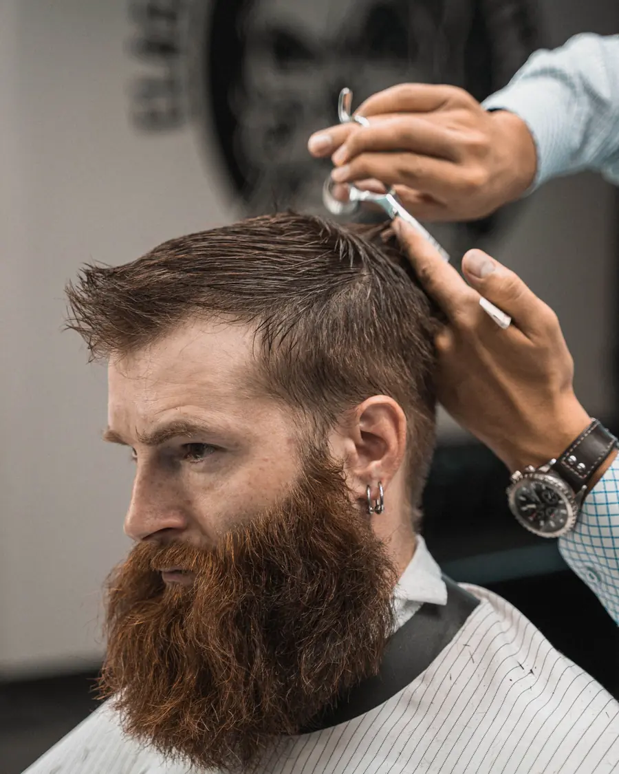 Barber shaping a client's long beard with scissors and comb