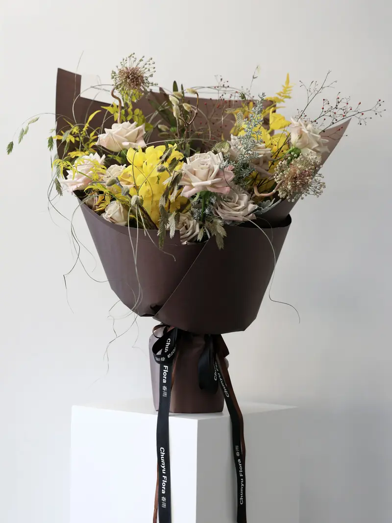 Bouquet of yellow roses, pale lisianthus and dried grasses in dark brown paper