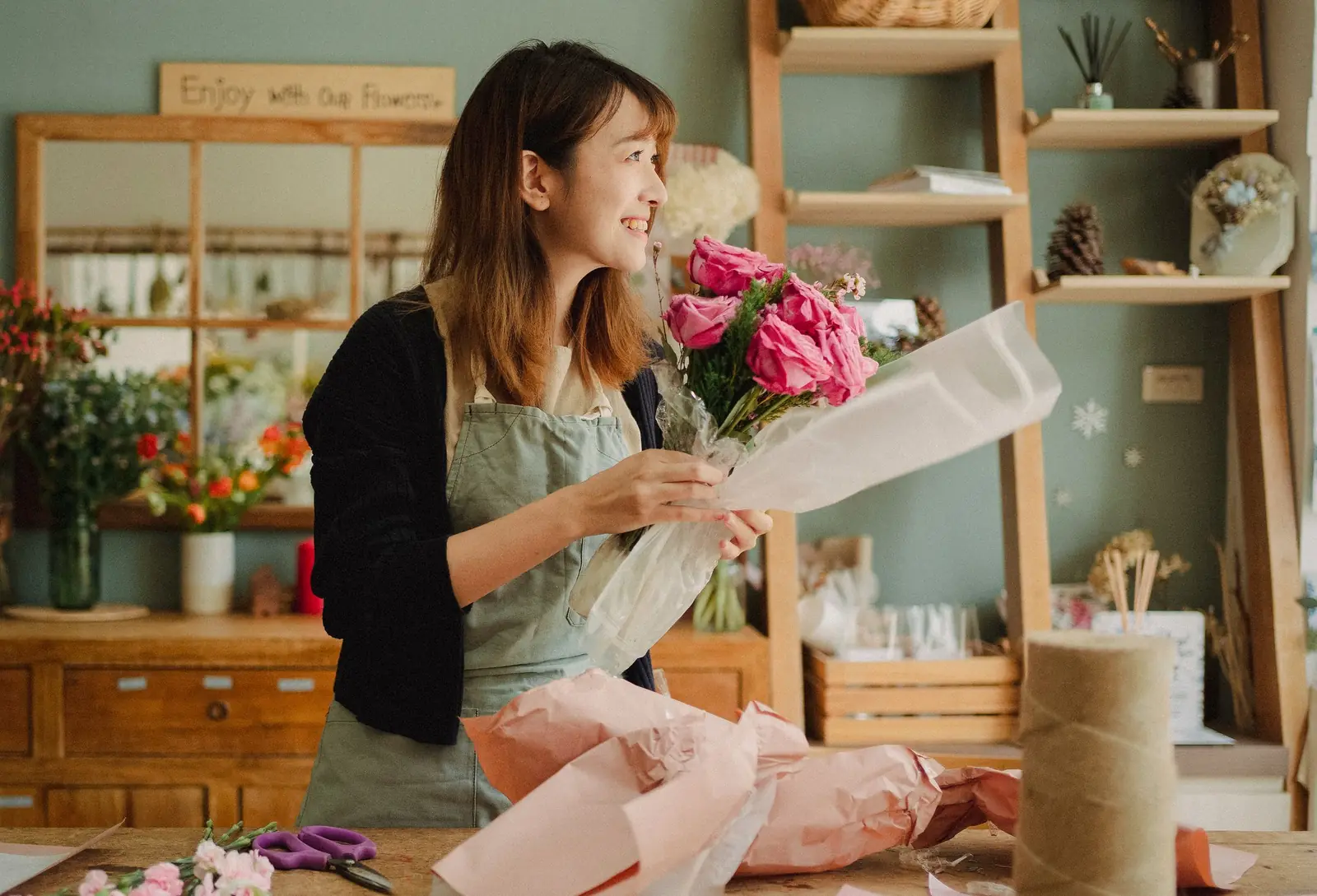 Florist smiling as she wraps a bouquet of pink roses in her shop