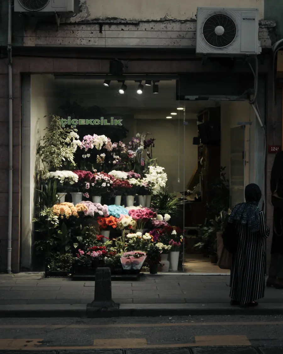 The shop front at dusk, with buckets of flowers lit up in the window
