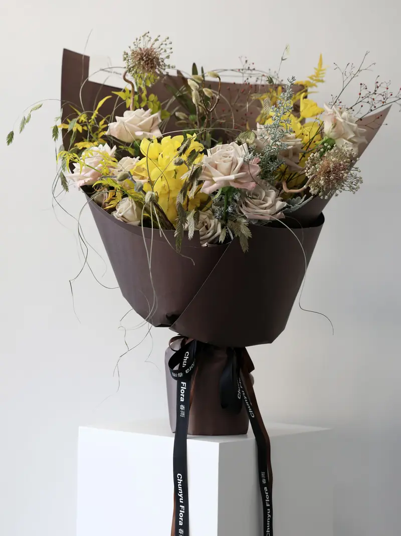 Loose wild-style bouquet with orange orchids, pale roses and grasses in brown paper