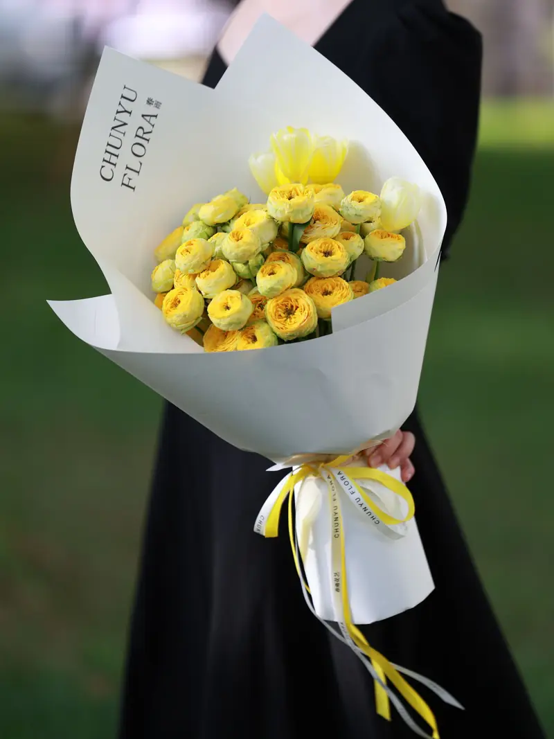 Round bouquet of yellow gerberas wrapped in white paper with a yellow ribbon