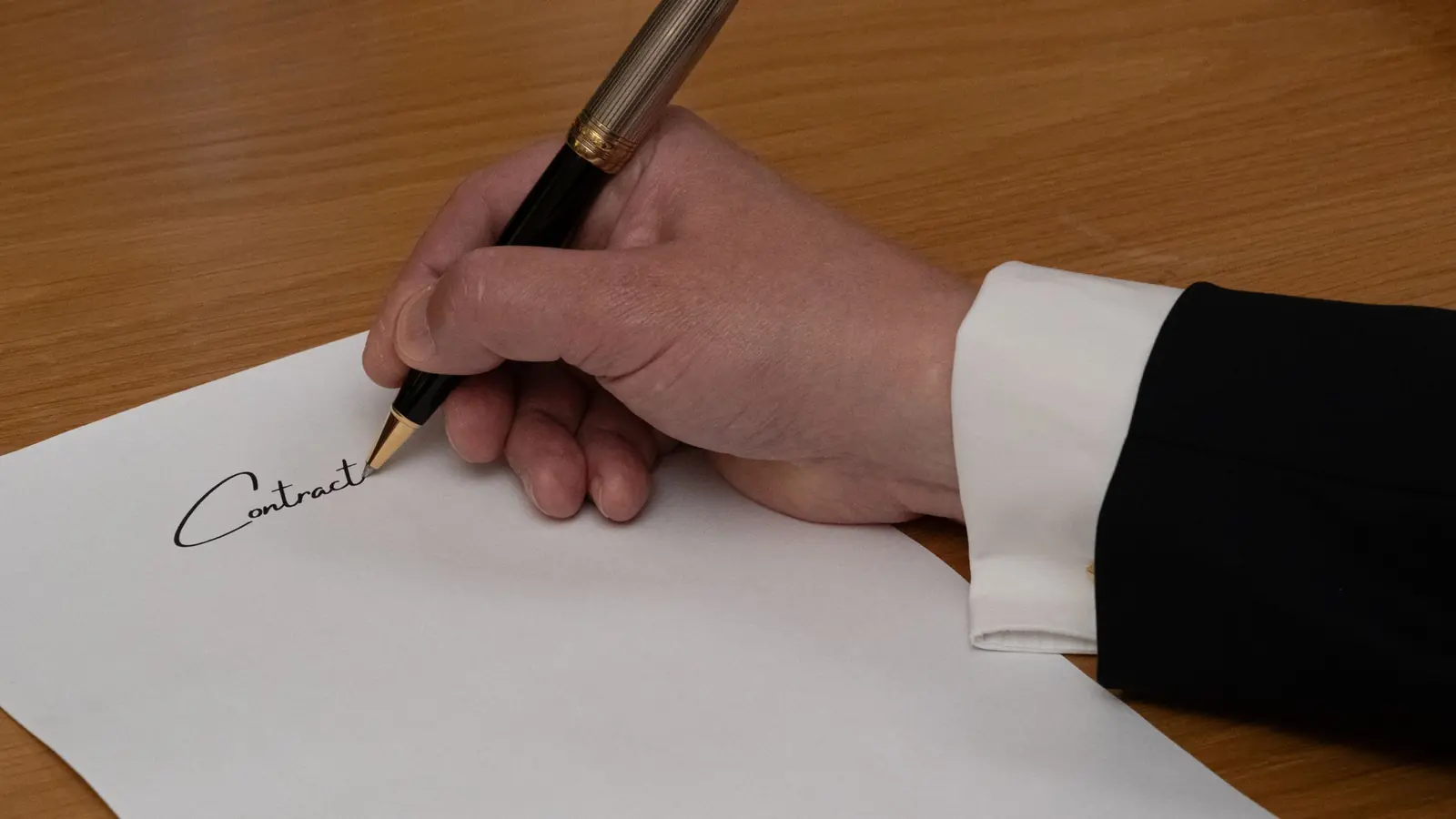 Hand signing a contract with a fountain pen on a wooden desk