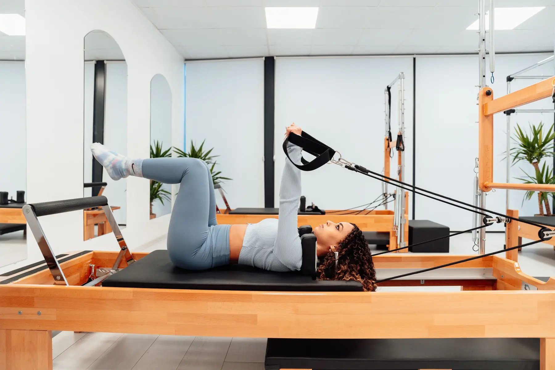 Woman doing a leg exercise on a wooden reformer in a bright studio