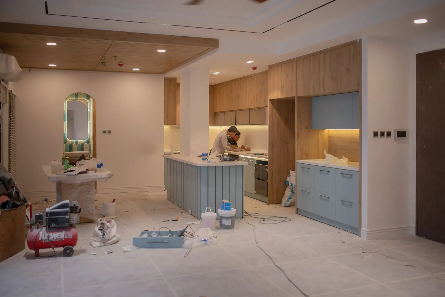 Kitchen mid-renovation with new wooden cabinets, dust sheets and tools on the floor