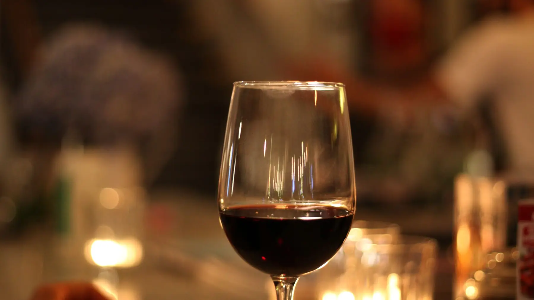 A glass of red wine on a candlelit bar counter